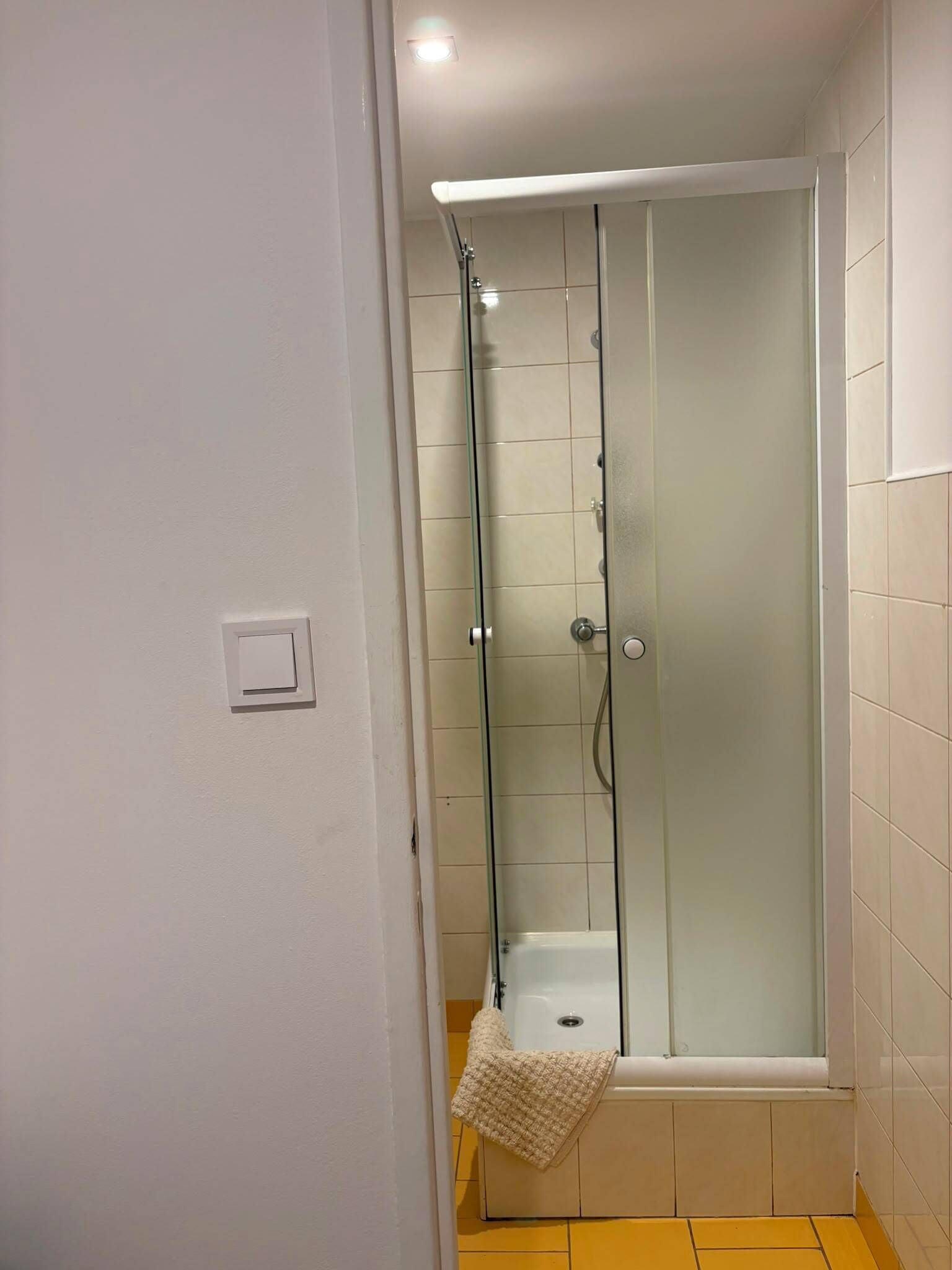 Eine begehbare Dusche mit Glastrennwand, weißem Boden und einem Handtuch, das an der Tür hängt.
