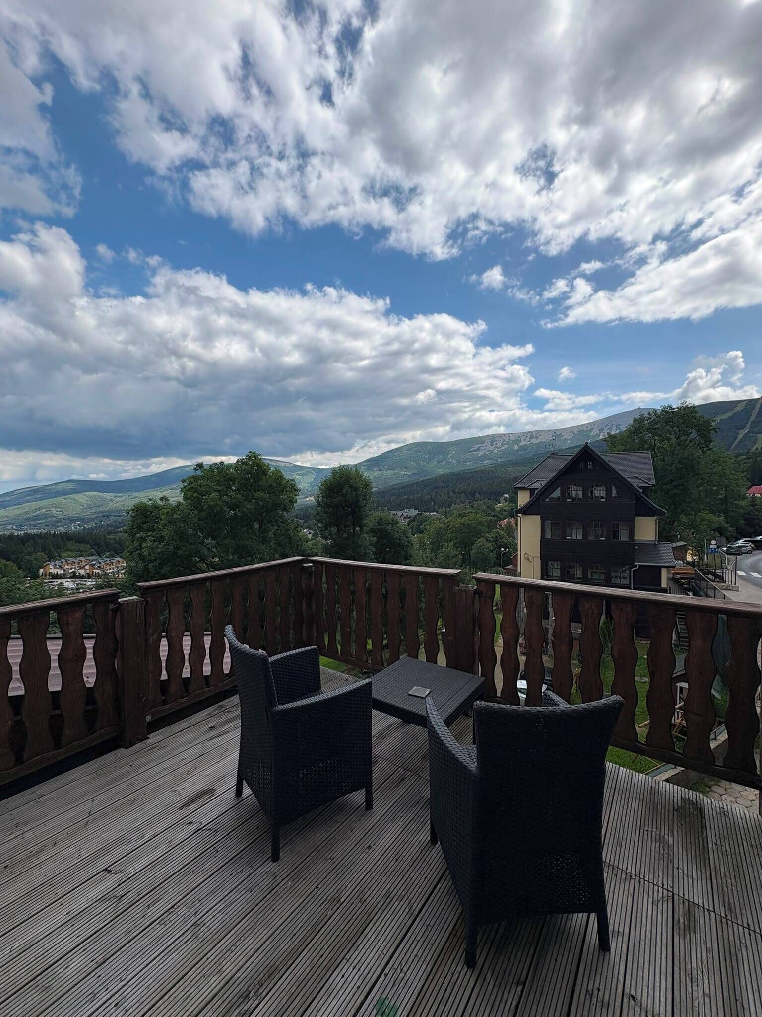 Terraza de madera con mobiliario exterior, con vista a un paisaje montañoso y un pueblo.