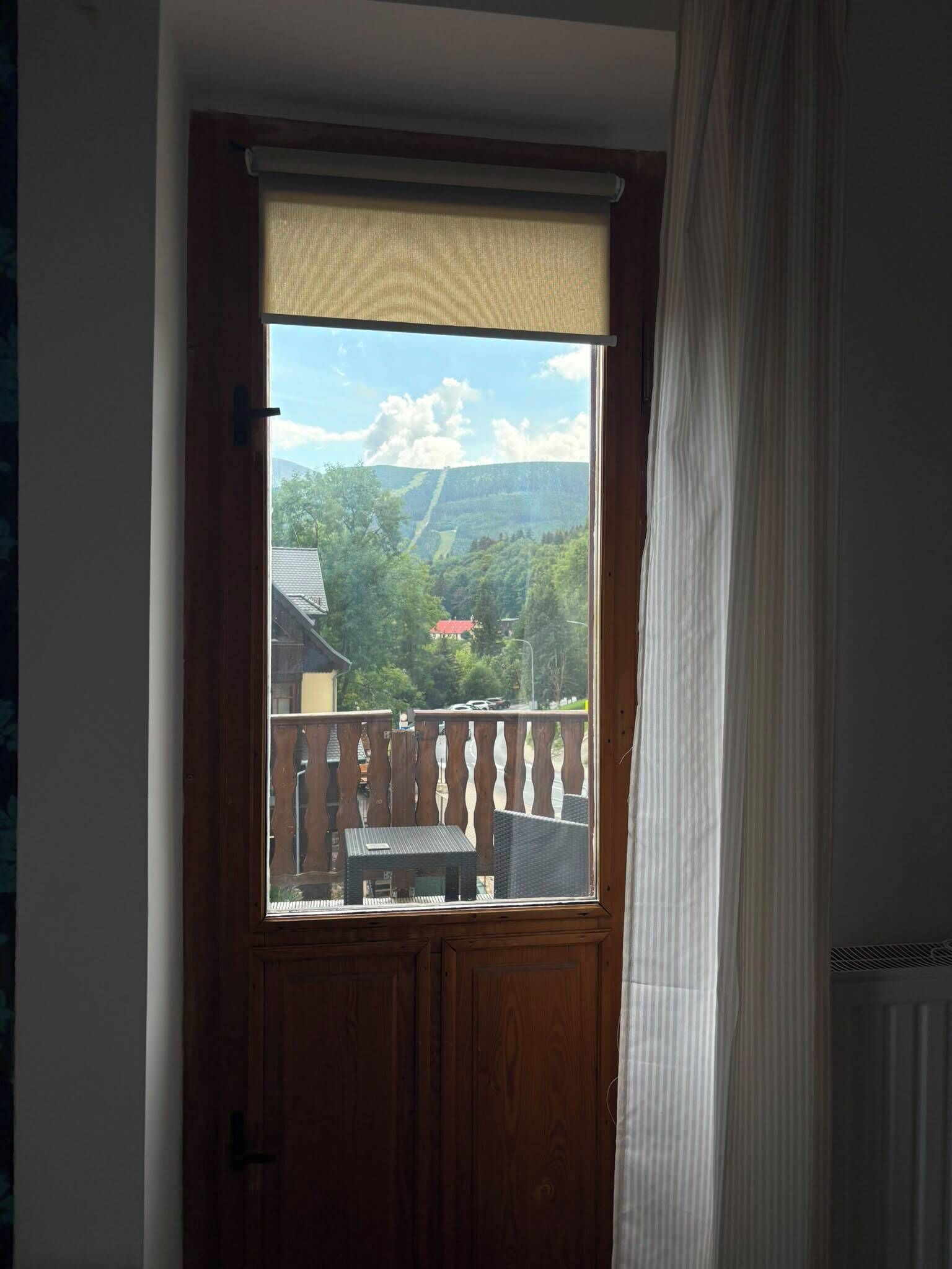 Une porte donnant sur un paysage montagneux, une clôture en bois et une table à l’extérieur.