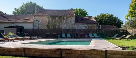 A swimming pool with lounge chairs, a stone building with a tiled roof, and a grassy yard.