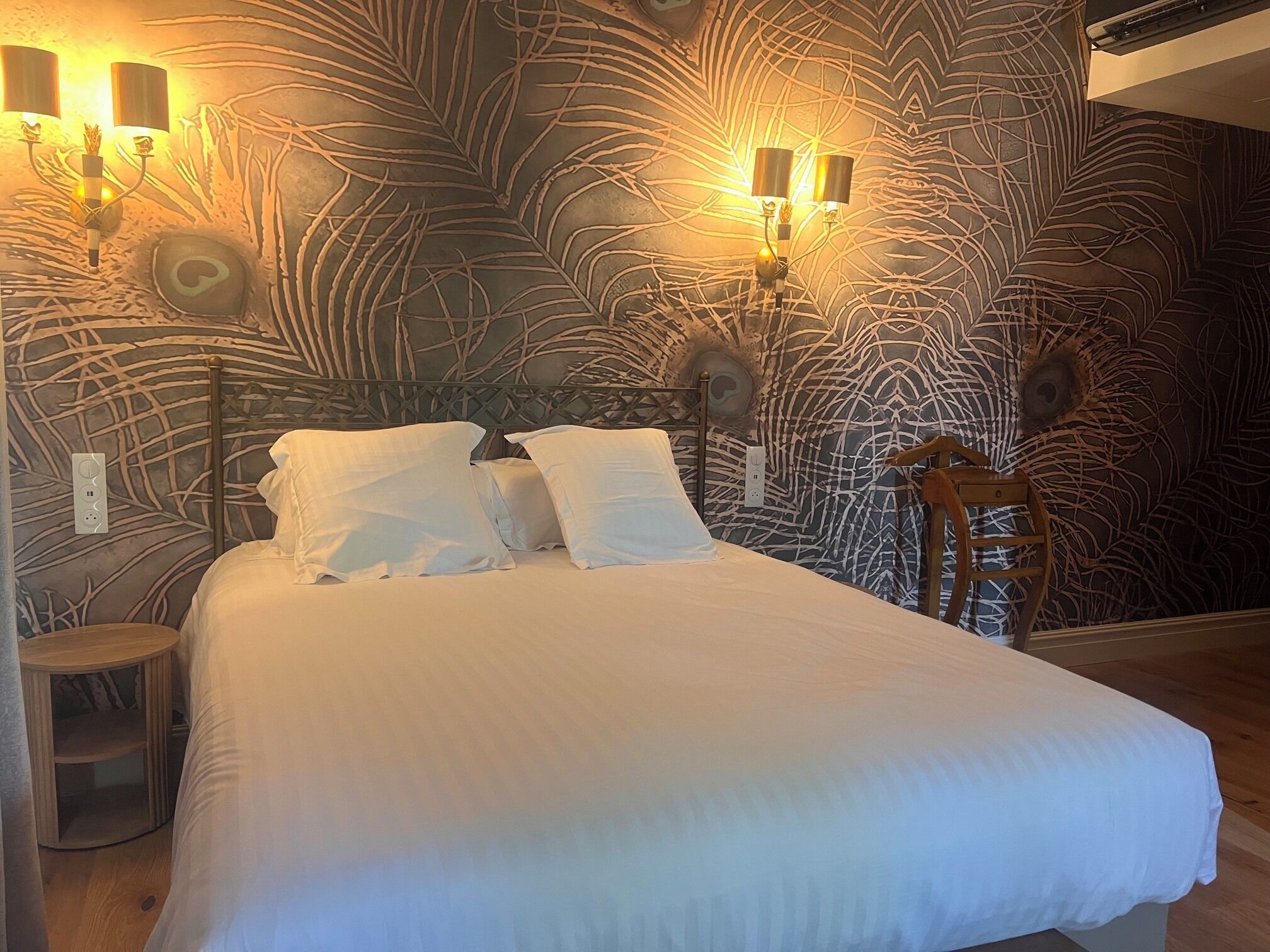 A bed with white bedding, a headboard with a leaf pattern, and wall-mounted lights.