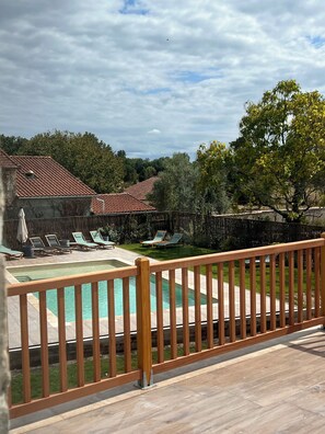A pool area with a wooden deck, lounge chairs, and a stone building in the background. - Le Groom Hôtel (Laprade)