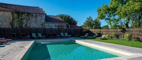Una piscina rectangular de aguas cristalinas, rodeada por una terraza de madera y un muro de piedra.