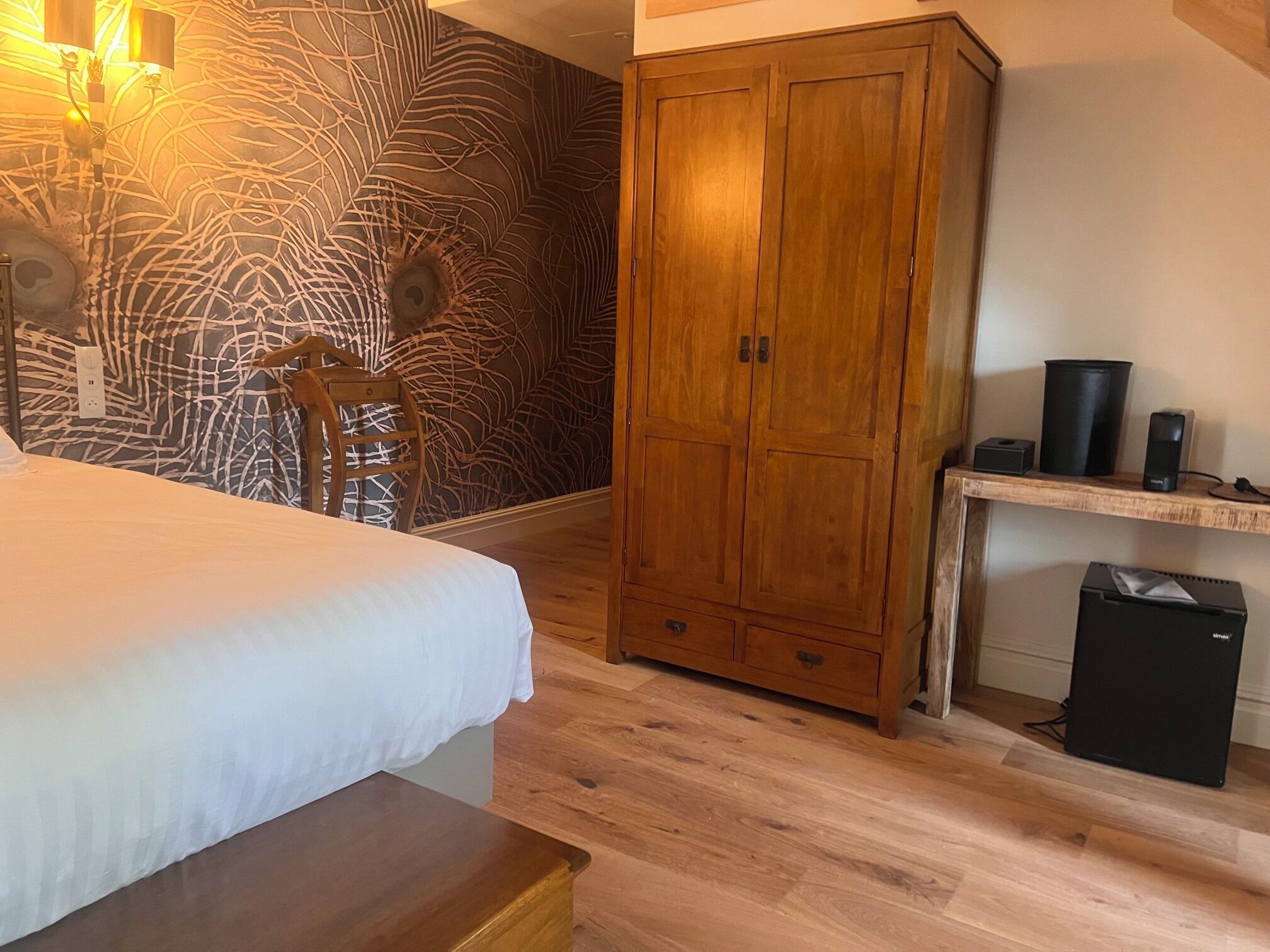 Une chambre à coucher comprenant un lit, une armoire en bois, un bureau avec un ordinateur et un mur décoré d’un motif.