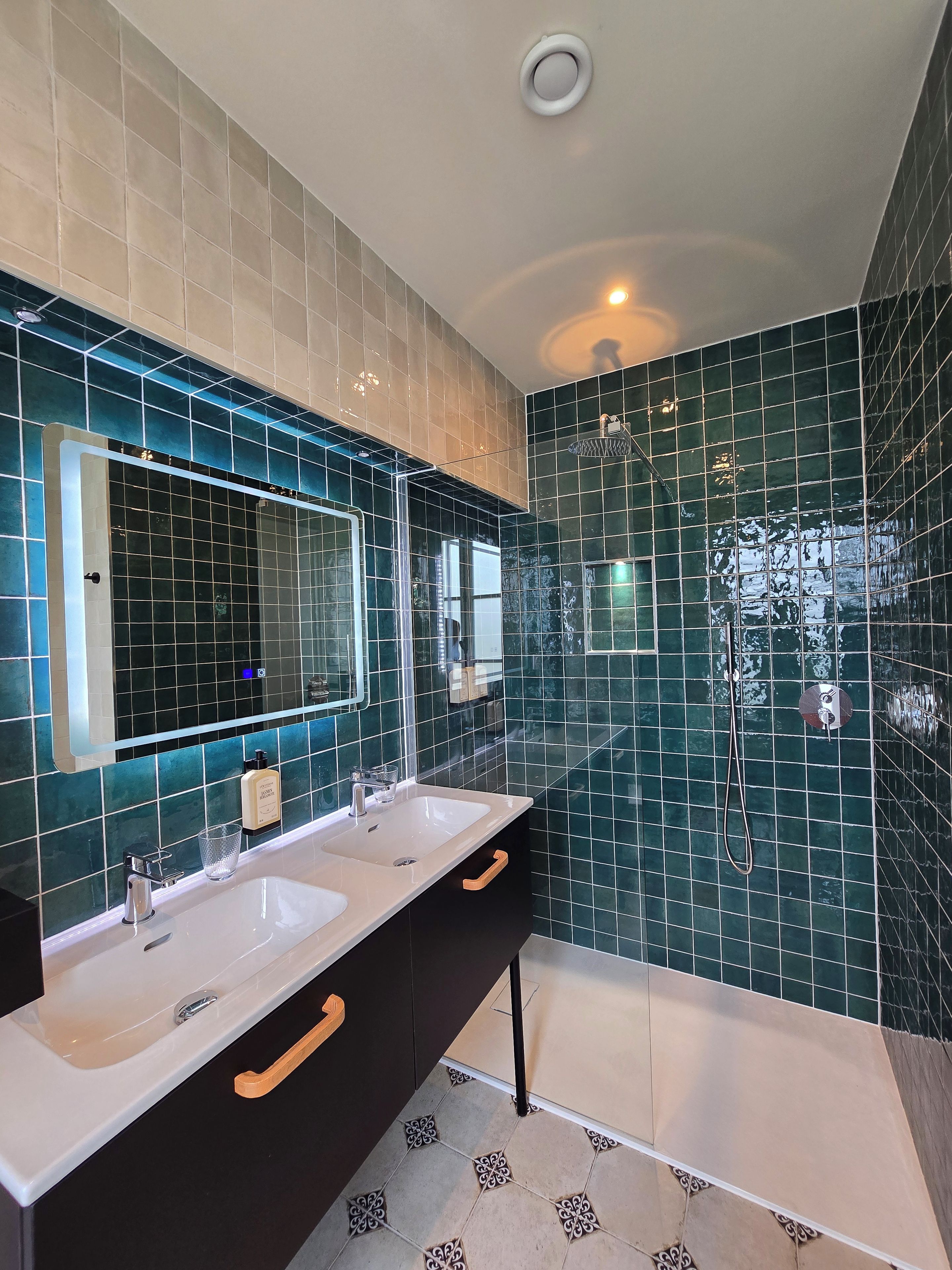 Une salle de bain avec deux lavabos, un miroir, une douche et un luminaire au plafond.