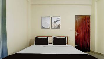 Une chambre d’hôtel avec un lit, deux œuvres d’art accrochées au mur, une porte en bois et une table de chevet.