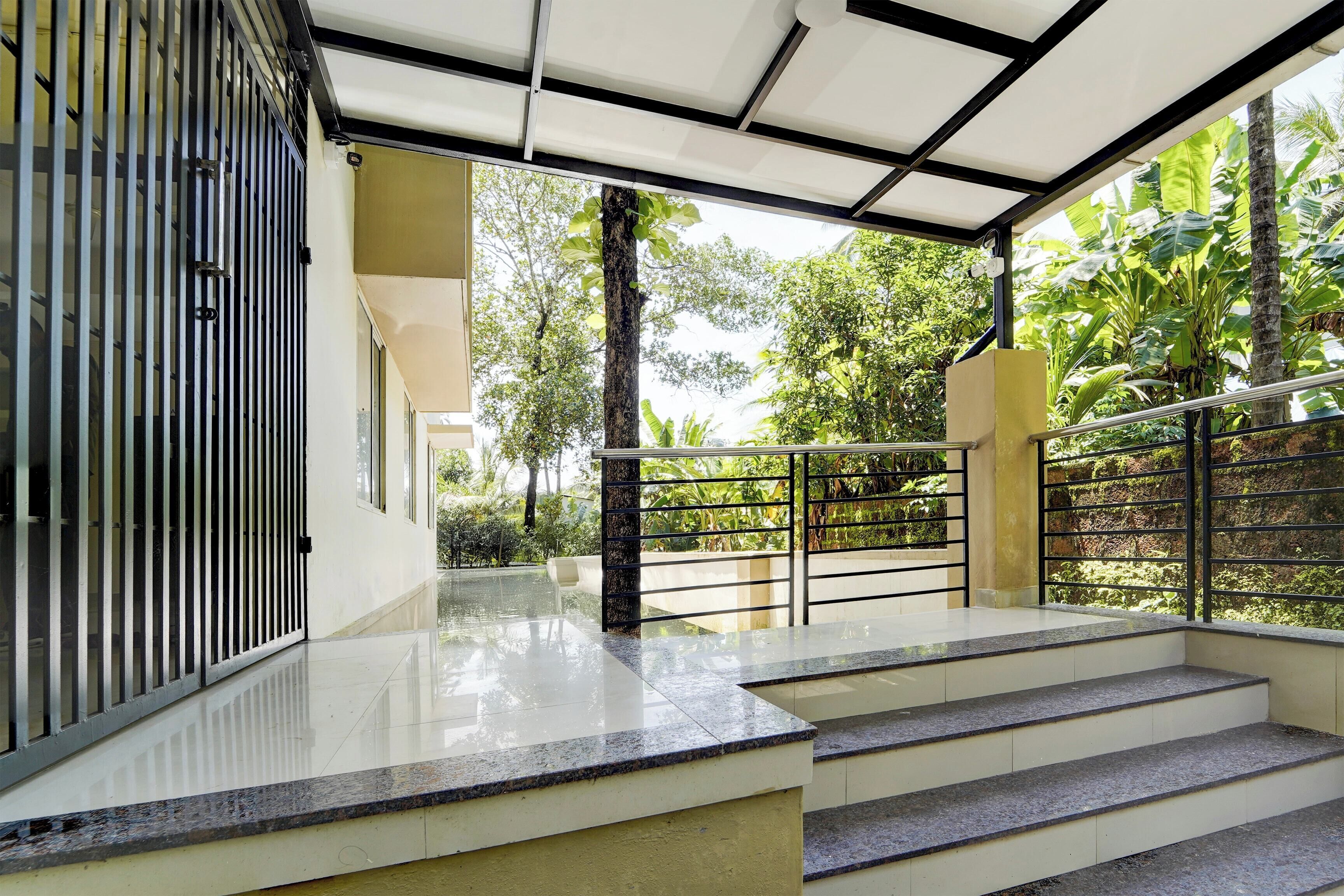 Un escalier extérieur moderne menant à un espace abrité, agrémenté d’un portail en métal et d’une végétation luxuriante en arrière-plan.