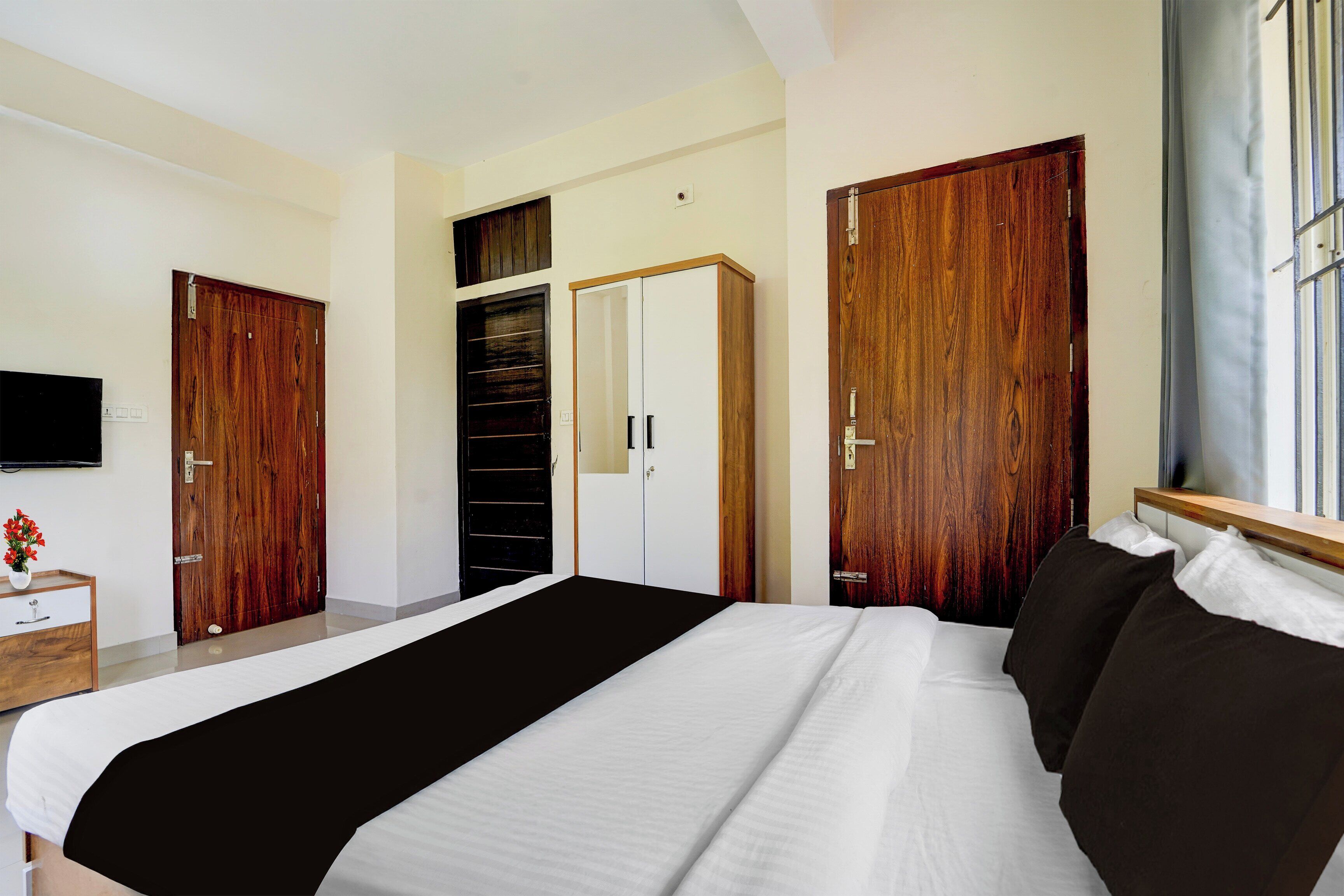 Une chambre à coucher avec un grand lit, une armoire en bois, un téléviseur fixé au mur et une fenêtre avec des rideaux.