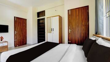 Une chambre à coucher avec un grand lit, une armoire en bois, un téléviseur fixé au mur et une fenêtre avec des rideaux.