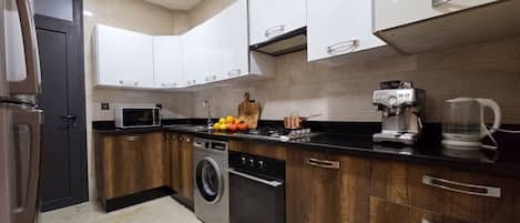 A modern kitchen with wooden cabinets, a stainless steel washing machine, a coffee maker, and a kettle.