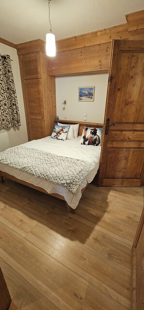 A wooden-framed room with a bed, a wooden door, and a wall-mounted light fixture. - L'Ecrin Alpin- Votre parenthèse alpine ski au pied aux Menuires- 4 chambres (Les Belleville)