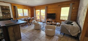 A wooden cabin interior with a dining area, seating, a TV, and a fireplace. - L'Ecrin Alpin- Votre parenthèse alpine ski au pied aux Menuires- 4 chambres (Les Belleville)