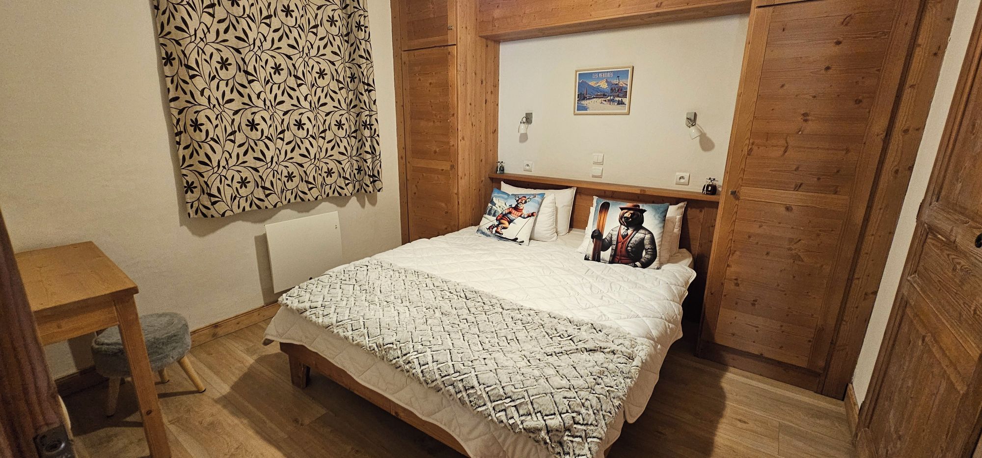 Une chambre avec un lit en bois, une décoration murale à motifs, un coussin sur le thème du ski et un tableau encadré accroché au mur.