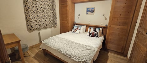 A bedroom with a wooden bed, a patterned wall hanging, a ski-themed pillow, and a framed picture on the wall.