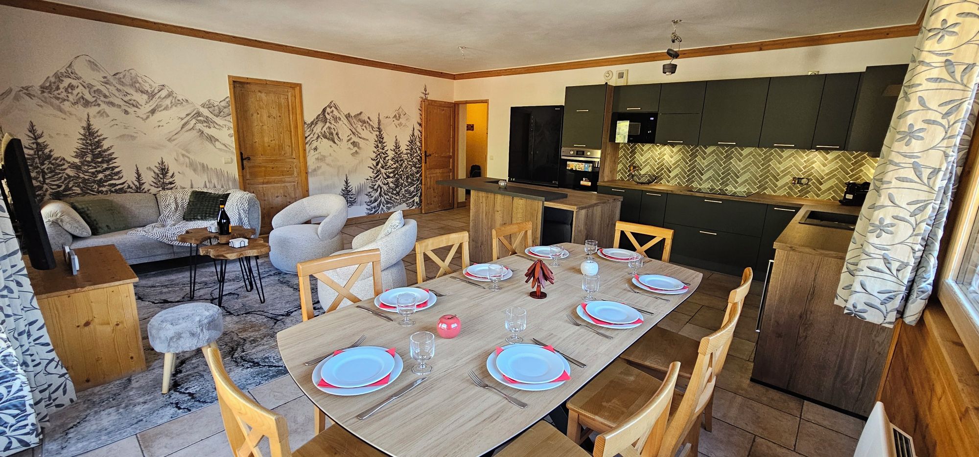 Un comedor con una mesa de madera dispuesta para cuatro personas, rodeada de sillas. Se observa una cocina con armarios oscuros y un salpicadero tipo espiga en el fondo.