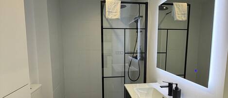 A modern bathroom with a toilet, a shower enclosure, a sink with a mirror, and recessed ceiling lights.