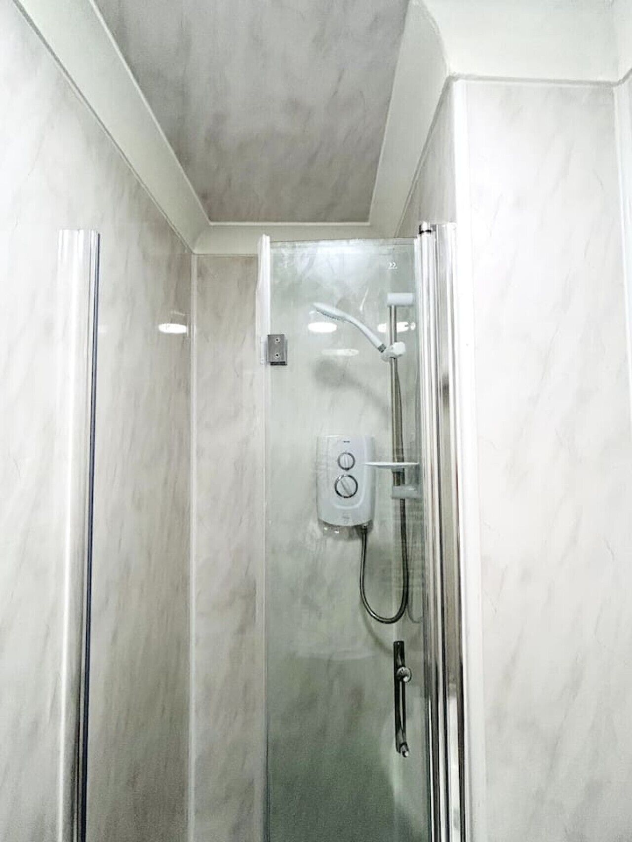 A glass-enclosed shower with a handheld showerhead and a wall-mounted control panel.
