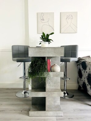 A modern, minimalist room with a grey console table, two bar stools, a potted plant, and two abstract wall art pieces. - Kensington Studio Gem - Rare find by Holland Park (Greater London)
