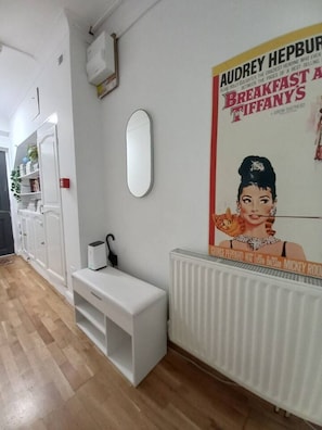 A hotel room with a white radiator, a white bench, a white shelf with books, and a poster on the wall. - Kensington Studio Gem - Rare find by Holland Park (Greater London)