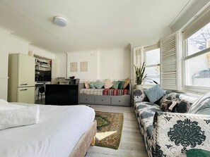 Habitación de hotel con cama, sofá, escritorio, kitchenette y ventana con persianas.