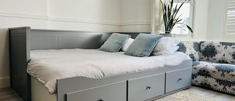 A modern bedroom with a grey bed, a patterned rug, and a window with blinds.