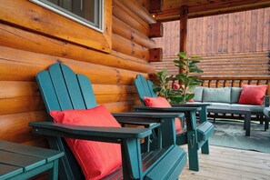 Eine Blockhütte mit Veranda, ausgestattet mit Adirondack-Stühlen und einer Couch mit Kissen.