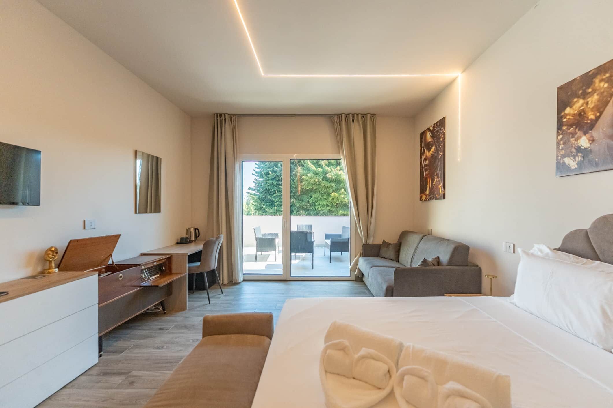 Ein modernes Hotelzimmer mit Bett, Schreibtisch, Sofa und einem Balkon mit Gartenmöbeln.