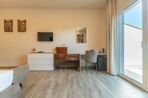 A modern hotel room with a flat-screen TV, a wooden desk, a chair, a sofa, and a large window. - Suite with a terrace overlooking the lake | Lagorá – C7 (San Giuliano Milanese)