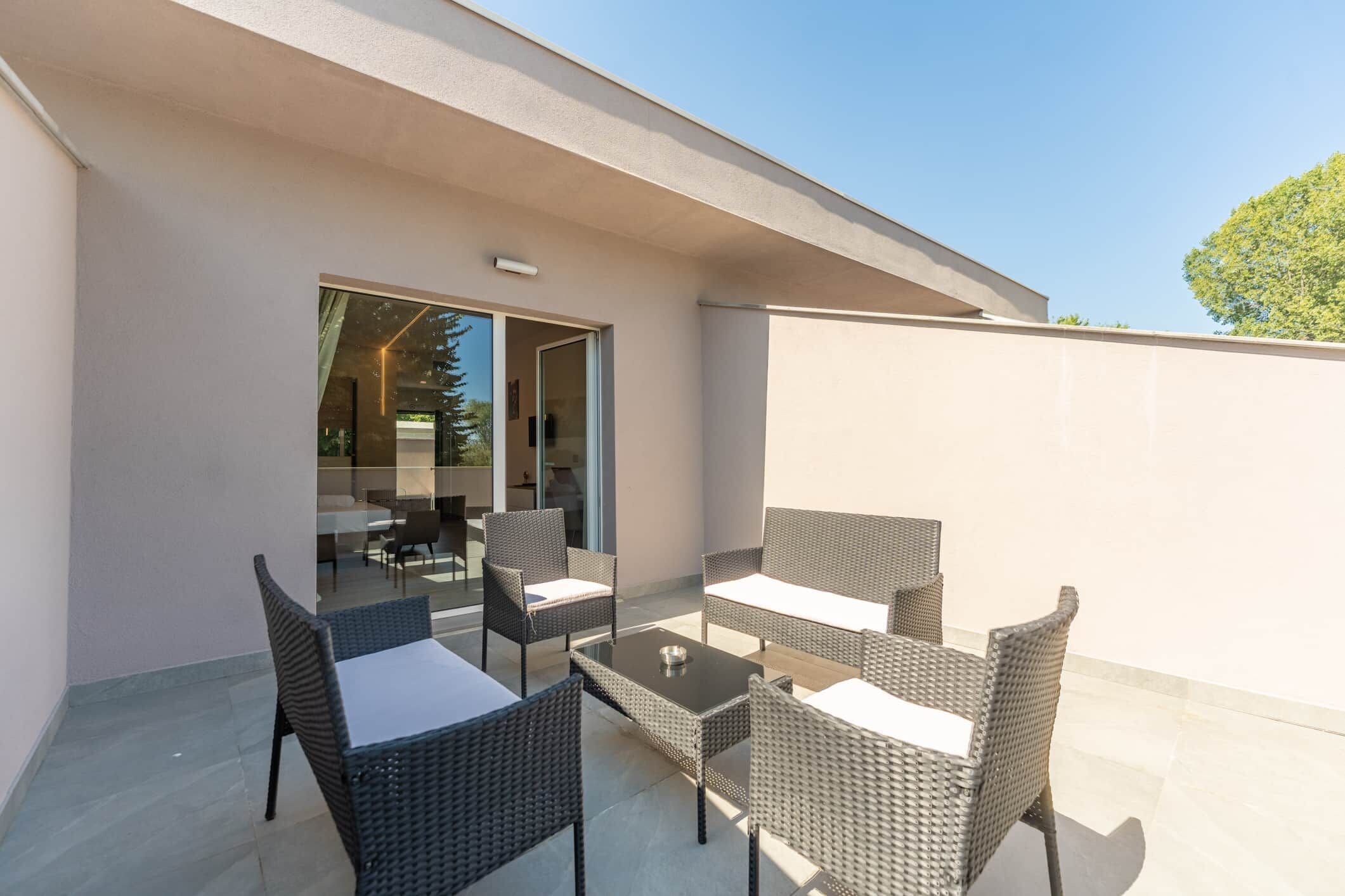 Un patio exterior con mobiliario de mimbre y un ventanal que da a un espacio interior.