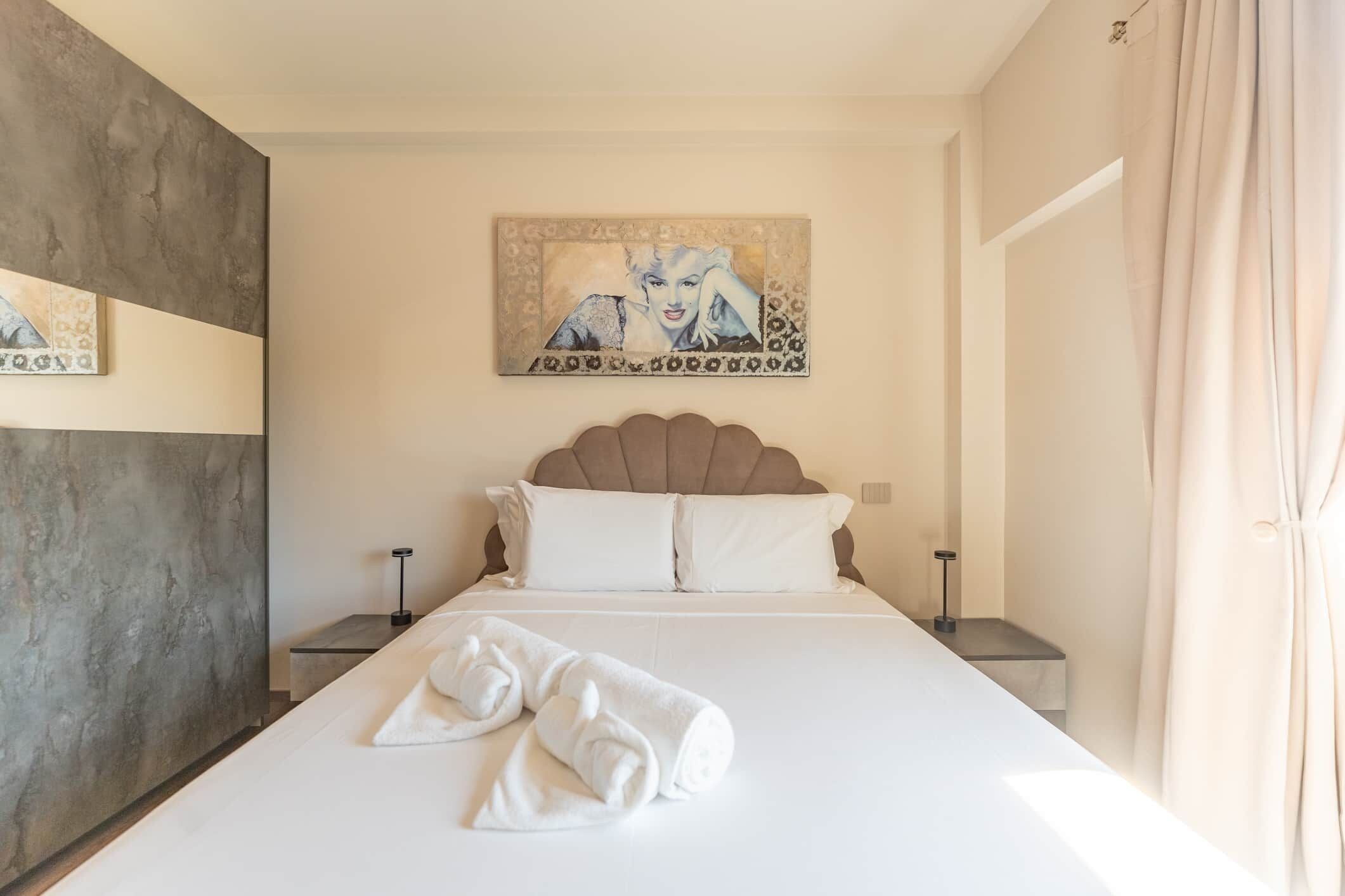 Ein Hotelzimmer mit einem großen Bett, einem Kopfteil, zwei Nachttischen, einem Wandbild und einem Handtuch auf dem Bett.