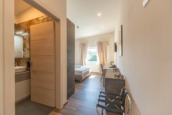 Ein modernes Hotelzimmer mit einem Holzschrank, einem Bett, einem Schreibtisch mit Stuhl und einem Vorhangfenster.
