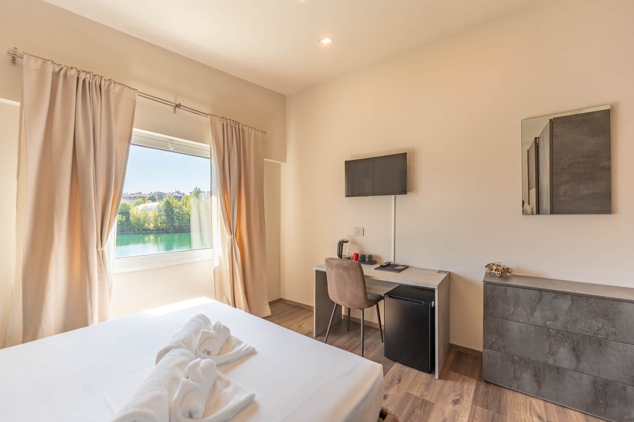 Una habitación de hotel con cama, escritorio, silla, televisor y vista al lago.