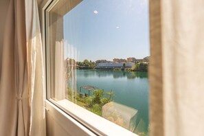 Blick durch ein Fenster auf einen ruhigen See mit Gebäuden im Hintergrund.