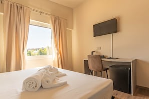 Ein Hotelzimmer mit Bett, Schreibtisch, Sessel, Fernseher und Blick auf die Stadt.