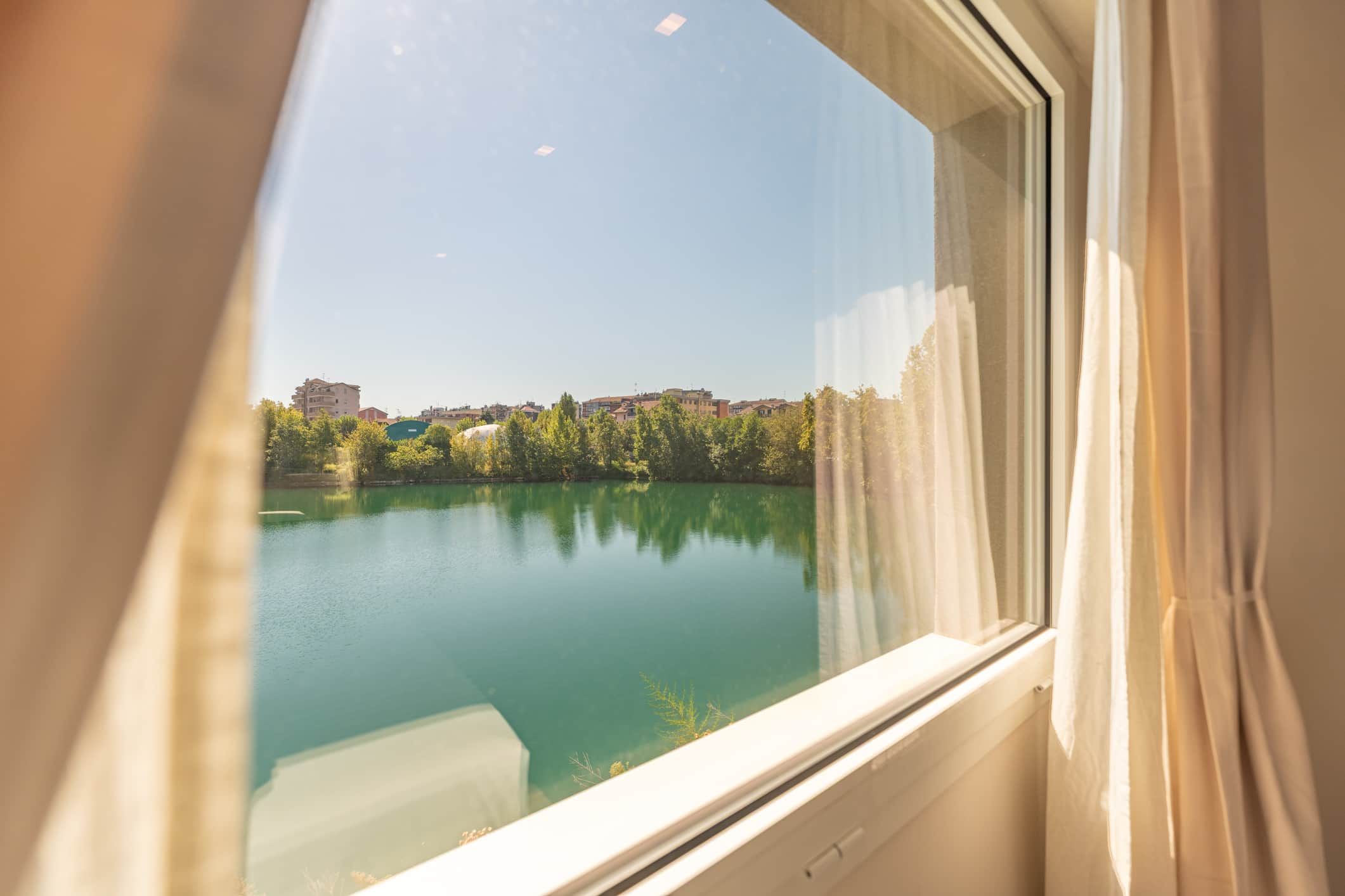 Blick durch ein Fenster, der einen klaren See und Gebäude in der Ferne widerspiegelt.