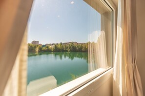 Blick durch ein Fenster, der einen klaren See und Gebäude in der Ferne widerspiegelt.