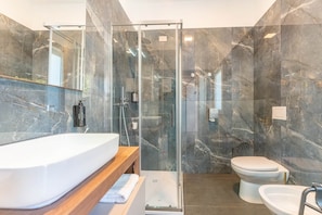 A modern bathroom with a glass-enclosed shower, a white sink, and a toilet.