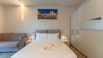 A hotel room with a bed, a sofa, a nightstand with a lamp, and a painting on the wall.