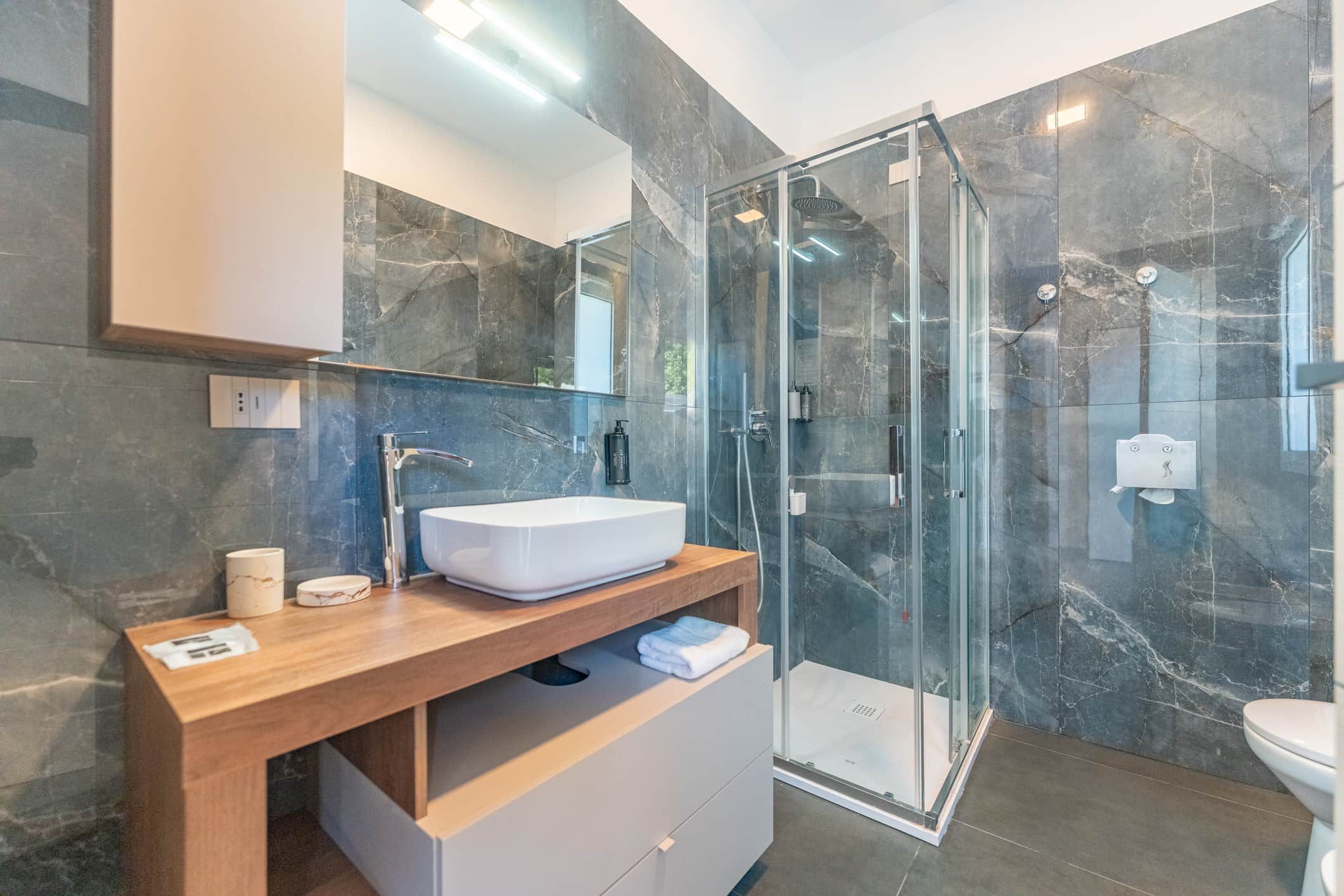 Un baño moderno con ducha envuelta en vidrio, un lavabo blanco y un mueble de tocador de madera.
