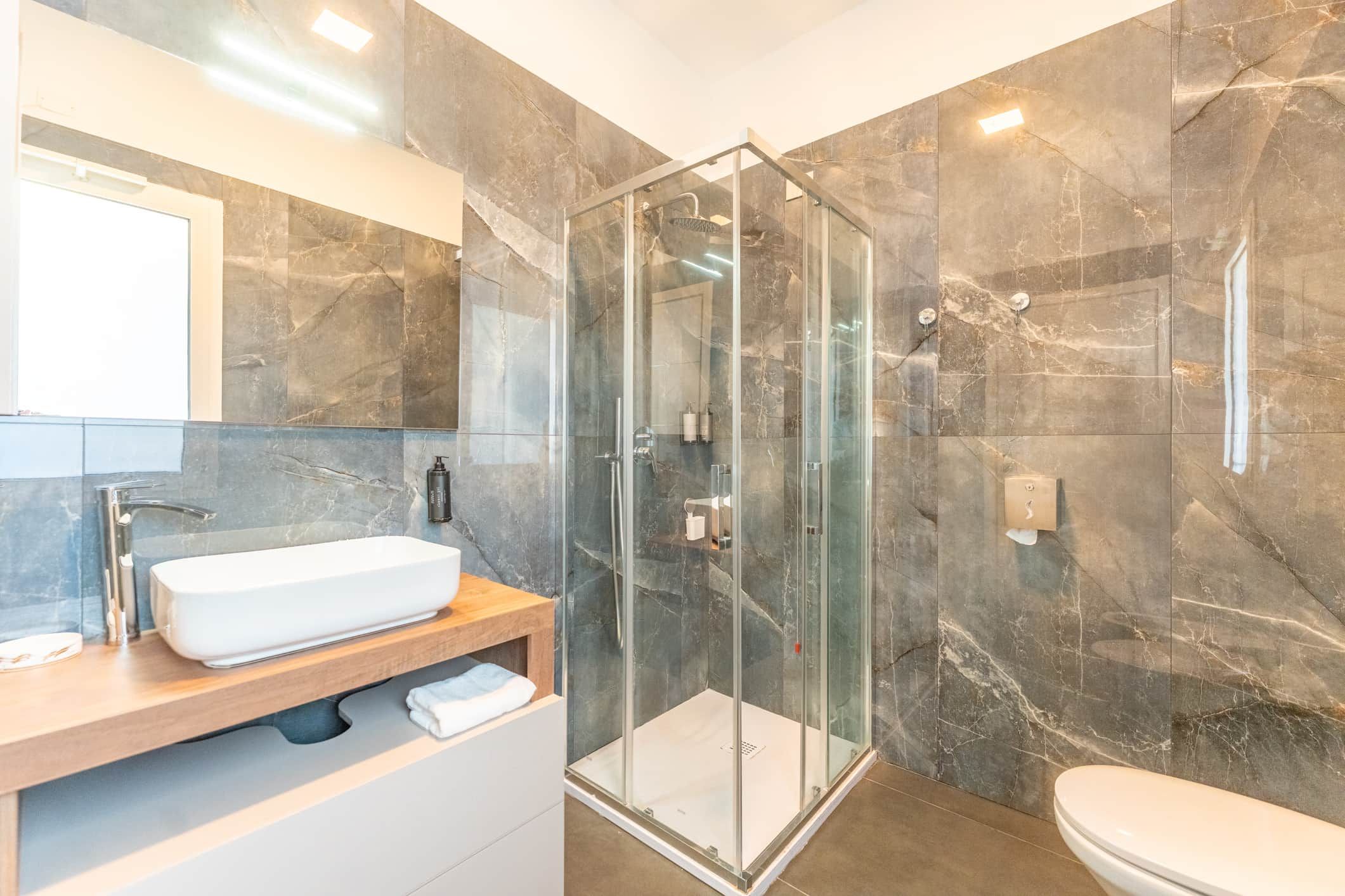 Ein modernes Badezimmer mit einer gläsernen Duschkabine, einem weißen Waschbecken und einer Wand mit Marmorplatten.