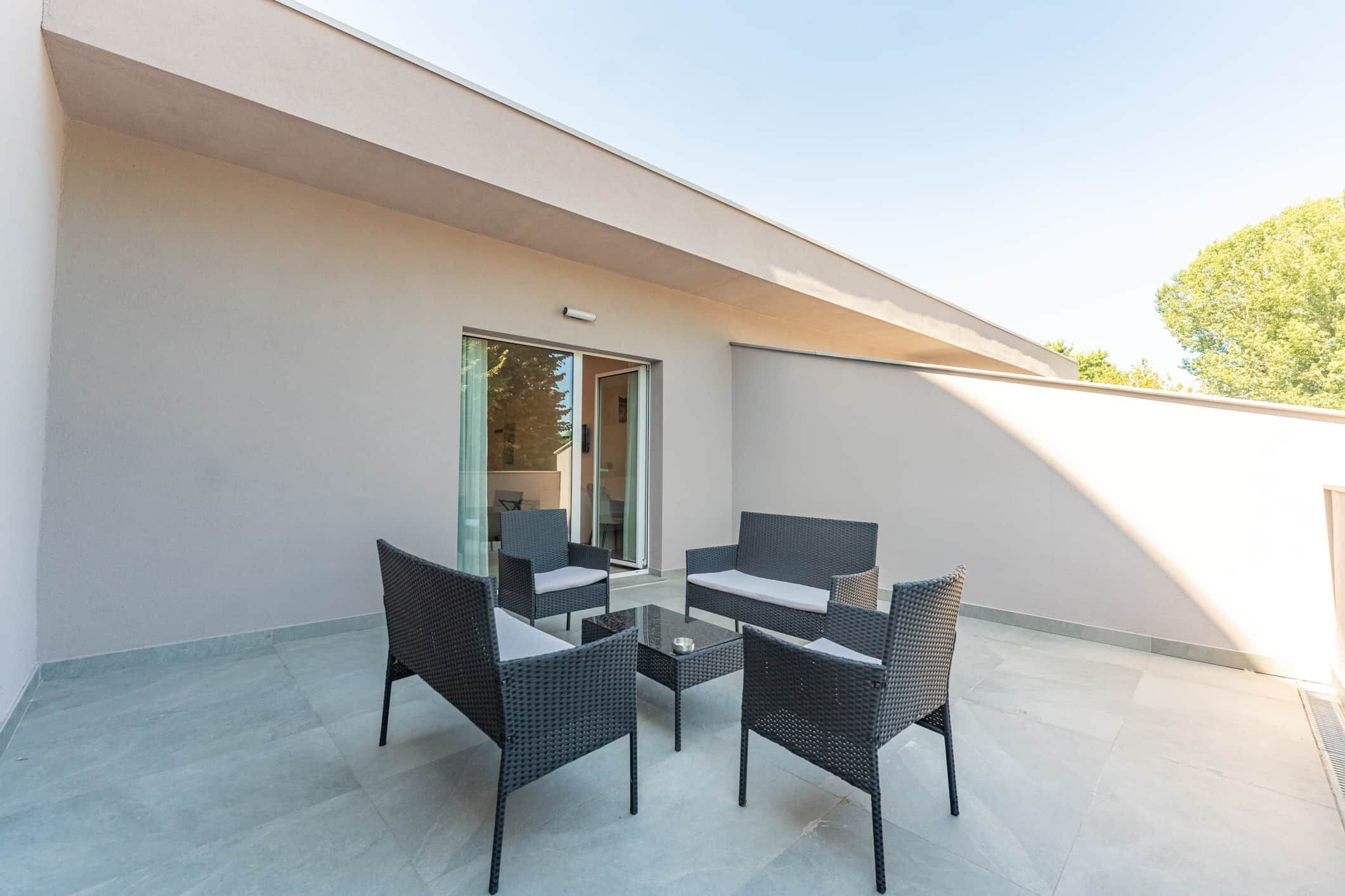 A modern outdoor seating area with a glass door leading to an interior space, featuring a table and four chairs.