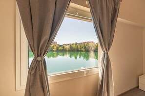 Una habitación con ventana que da a un lago tranquilo y edificios.