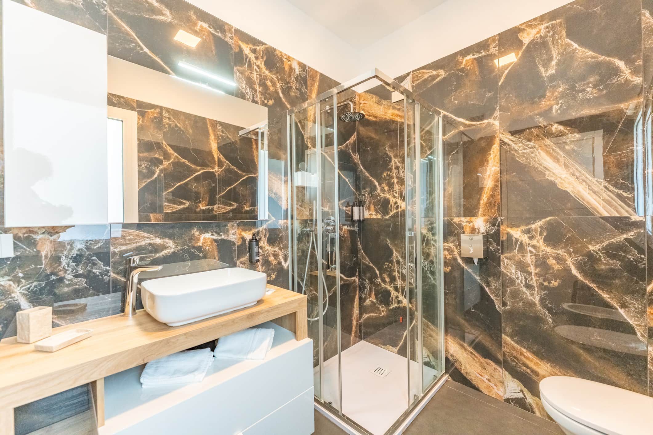 Un bagno moderno con doccia vetrata, lavandino bianco e pareti in marmo.