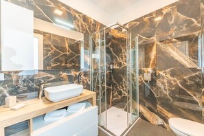 A modern bathroom with a glass-enclosed shower, a white sink, and marble walls. - Suite with a terrace overlooking the lake | Lagorá – C6 (San Giuliano Milanese)