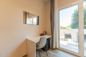 A room with a desk, chair, and a large window with curtains. - Suite with a terrace overlooking the lake | Lagorá – C6 (San Giuliano Milanese)