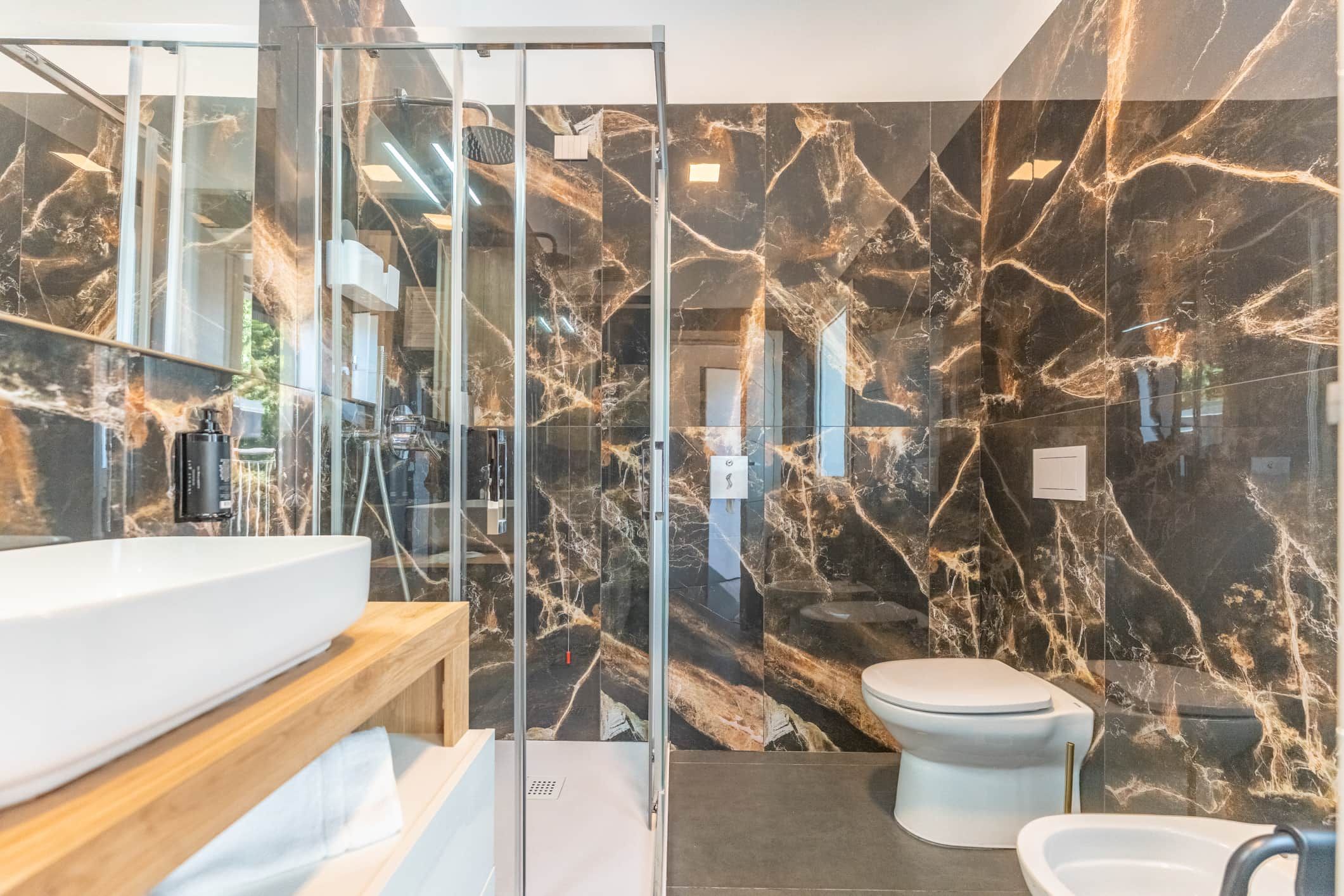 A modern bathroom with a glass shower enclosure, a marble backsplash, and a white toilet.
