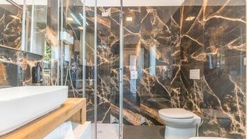 A modern bathroom with a glass shower enclosure, a marble backsplash, and a white toilet.