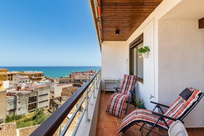 Un balcón con vistas al mar, dos sillas a rayas y una mesita.