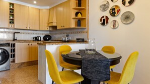 Une cuisine compacte avec des meubles en bois, un lave-linge encastré et un coin repas comprenant une table noire et des chaises jaunes.