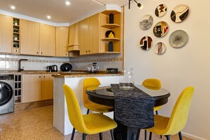 Eine kleine Küche mit Holzausbau, einer integrierten Waschmaschine und einem Essbereich mit einem schwarzen Tisch und gelben Stühlen.